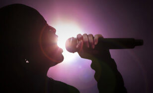 A silhouette of a female vocalist sings into a microphone