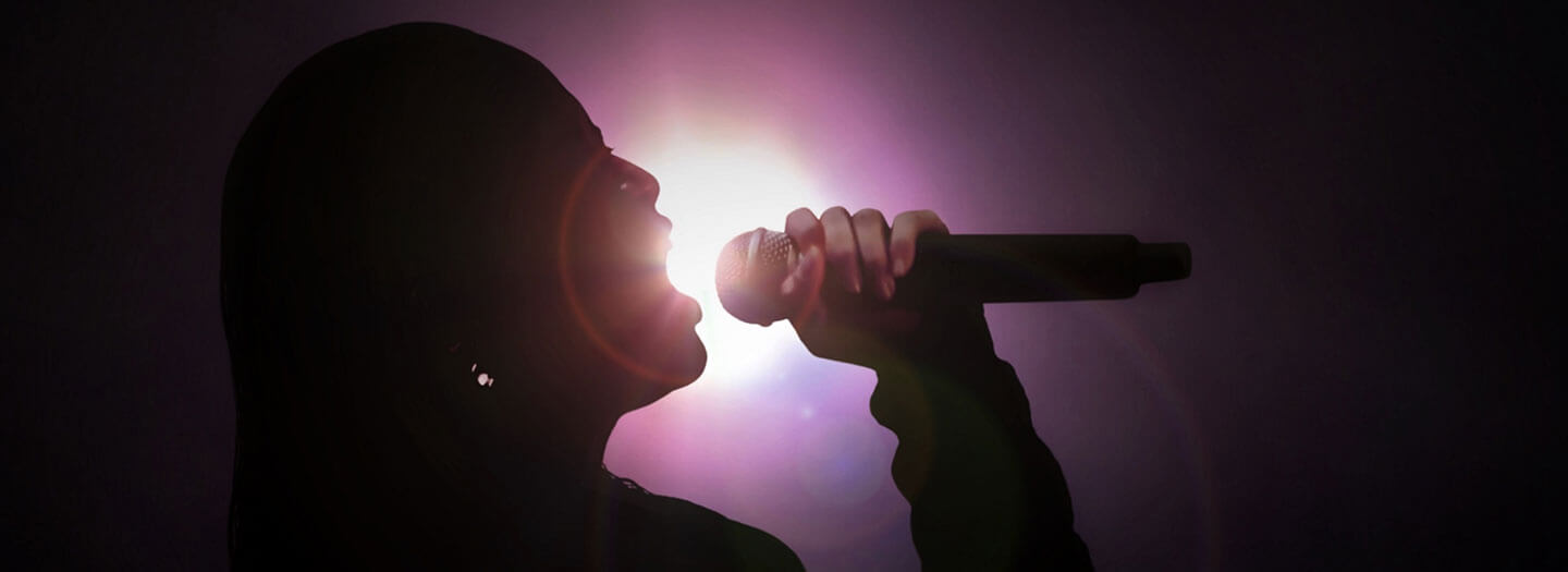 A silhouette of a female vocalist sings into a microphone