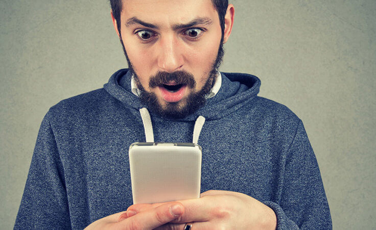 A man with a shocked face looks at his cellphone