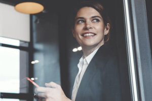 A businesswoman looks out of an office window while holding her cellphone