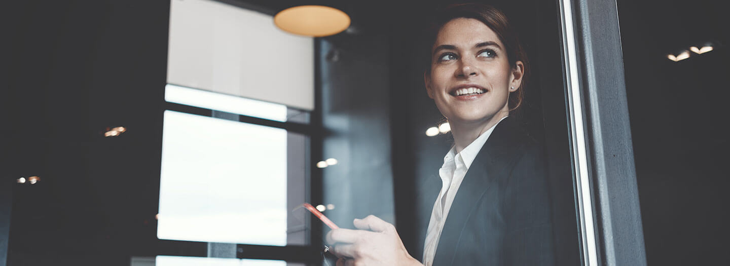 A businesswoman looks out of an office window while holding her cellphone