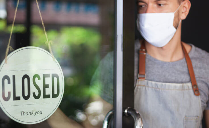 A man in a facemask looks at a closed sign on a restaurant door