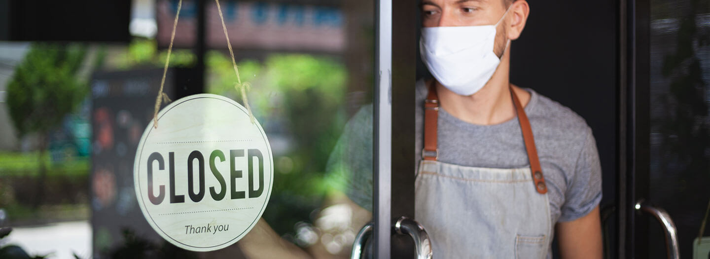 A man in a facemask looks at a closed sign on a restaurant door
