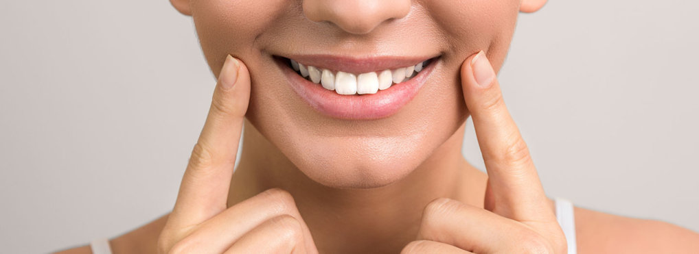 A woman smiles wide while placing her index fingers on both corners of her mouth
