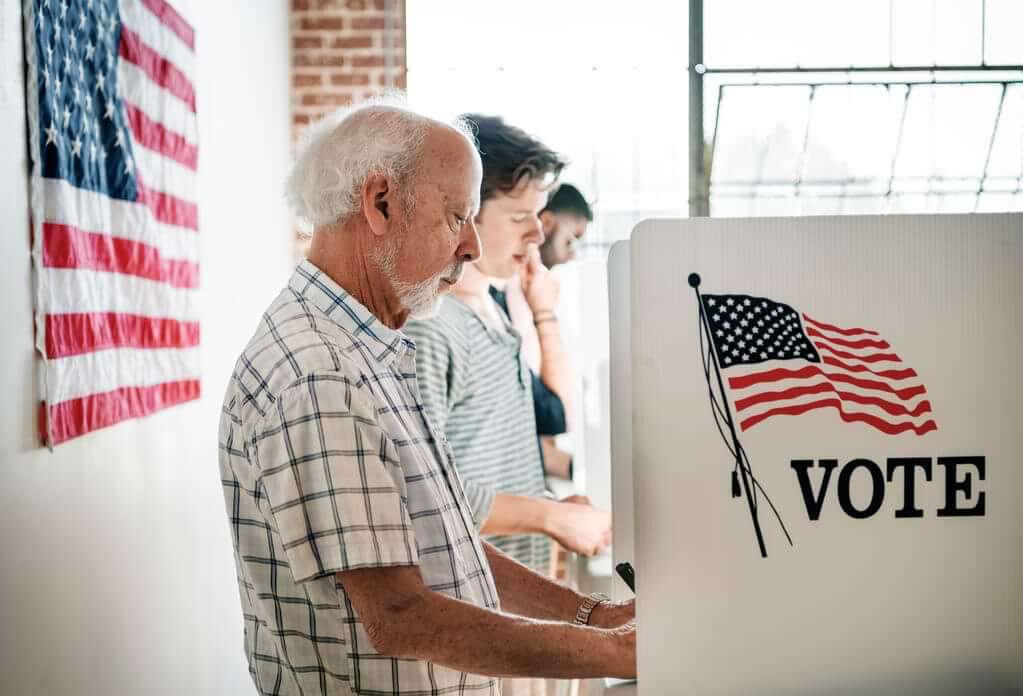 Several people voting at the polls, American flag in the background