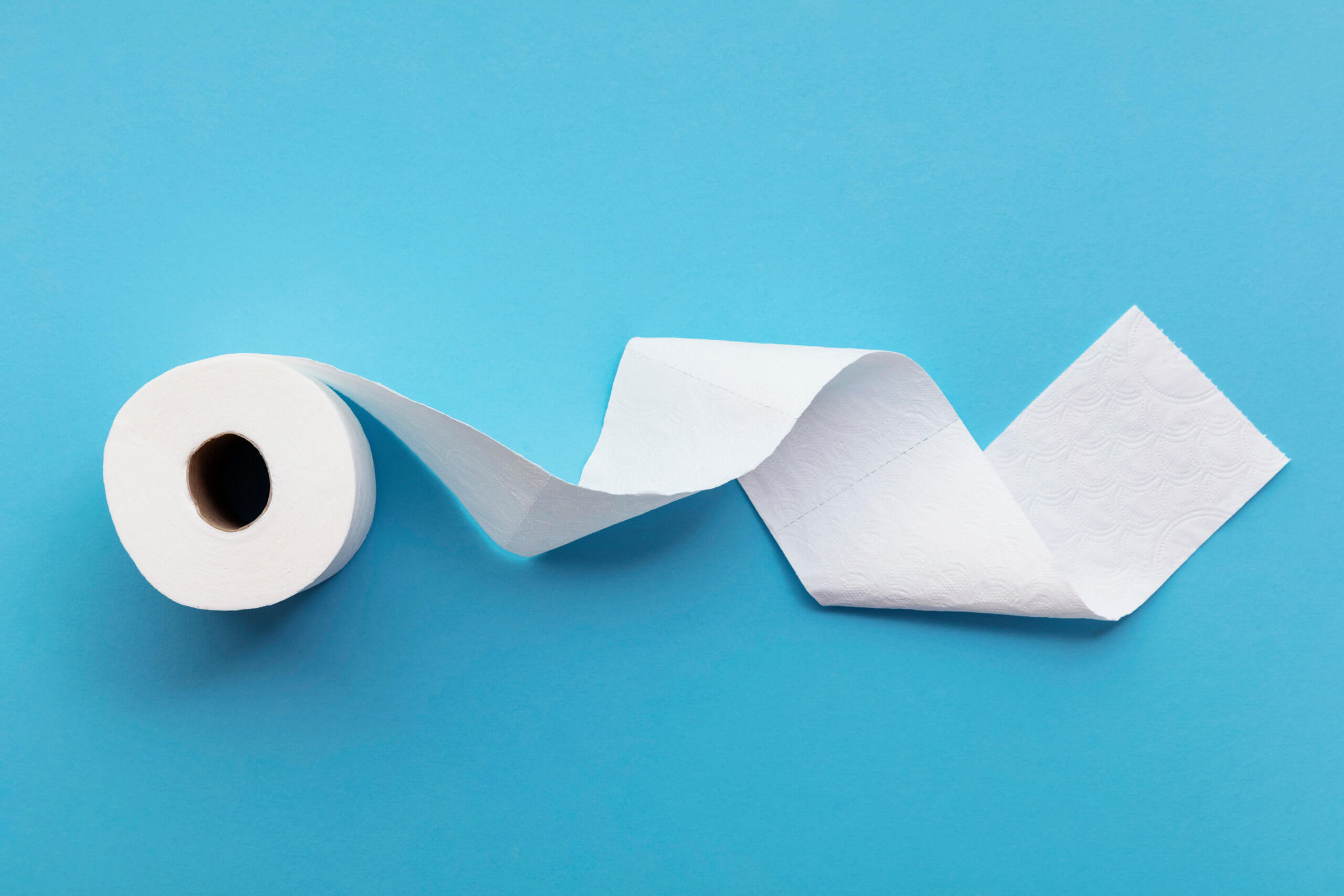 A single roll of toilet paper unrolled on a blue background © ink drop /stock.adobe.com
