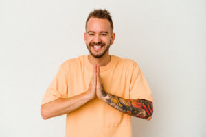 A young man holds his hands flat against each other in front him, his left arm covered in ink. What does the Bible say about tattoos?