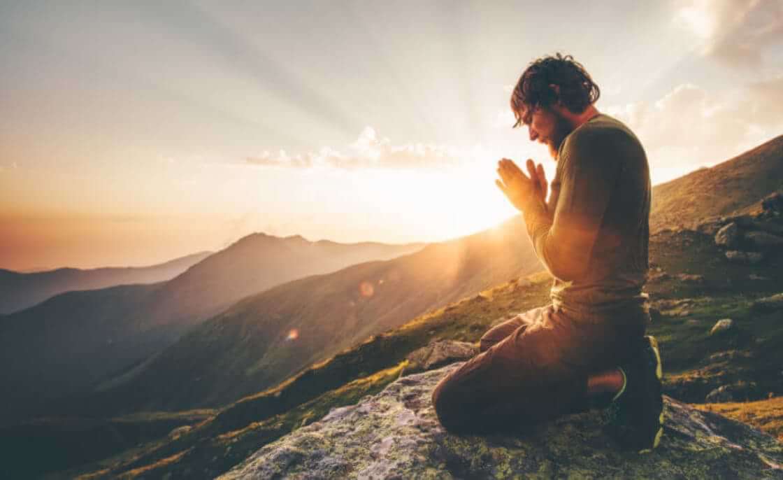 A man prays at sunset atop a high mountain. © EVERST /stock.adobe.com
