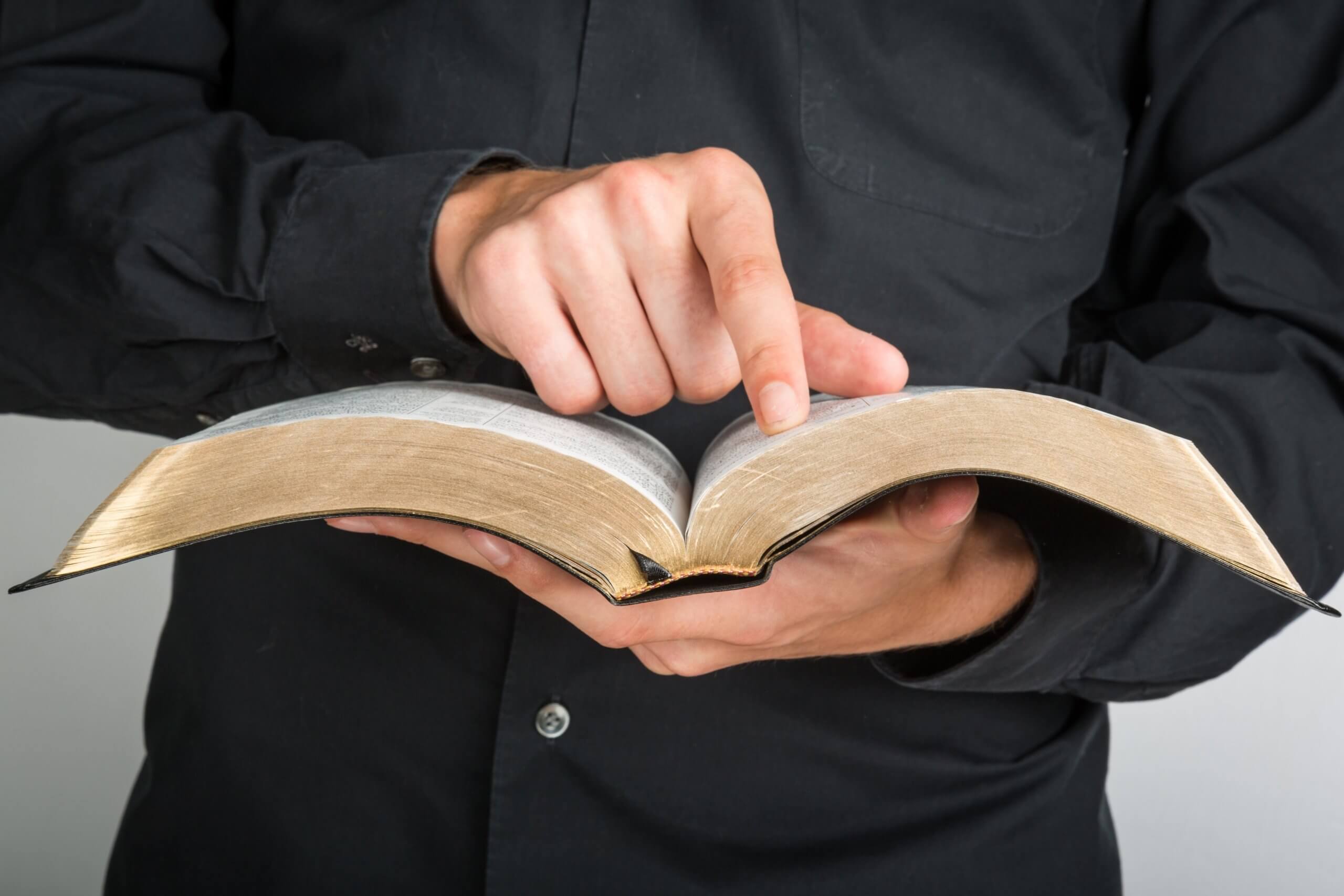 Stock photo: A pastor in a black shirt points to a passage in an open Bible. © BillionPhotos.com /stock.adobe.com