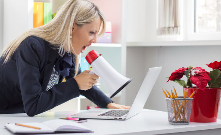 Stock photo: A businesswoman uses a megaphone to shout at her open laptop. © Kaspars Grinvalds /stock.adobe.com