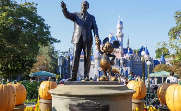 A statue of Walt Disney holding the hand of Mickey Mouse in front of the Disneyland castle in Anaheim, CA