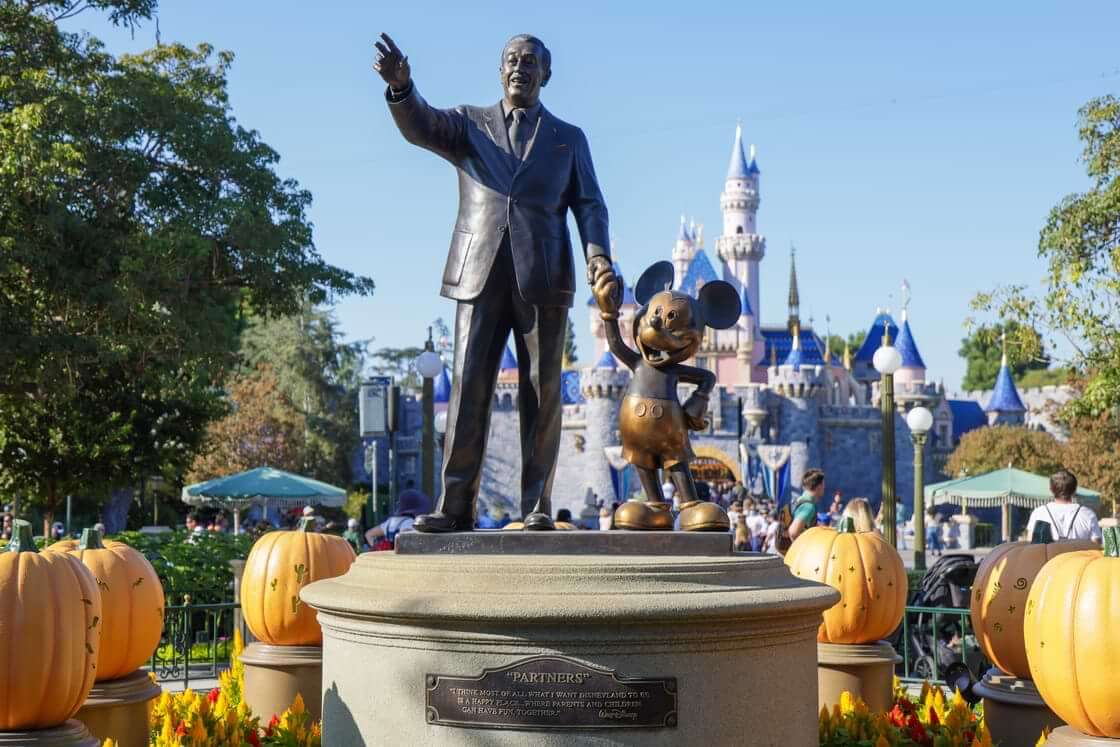 A statue of Walt Disney holding the hand of Mickey Mouse in front of the Disneyland castle in Anaheim, CA