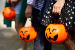 Three children at Halloween each hold their pumpkin candy buckets