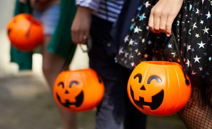 Three children at Halloween each hold their pumpkin candy buckets