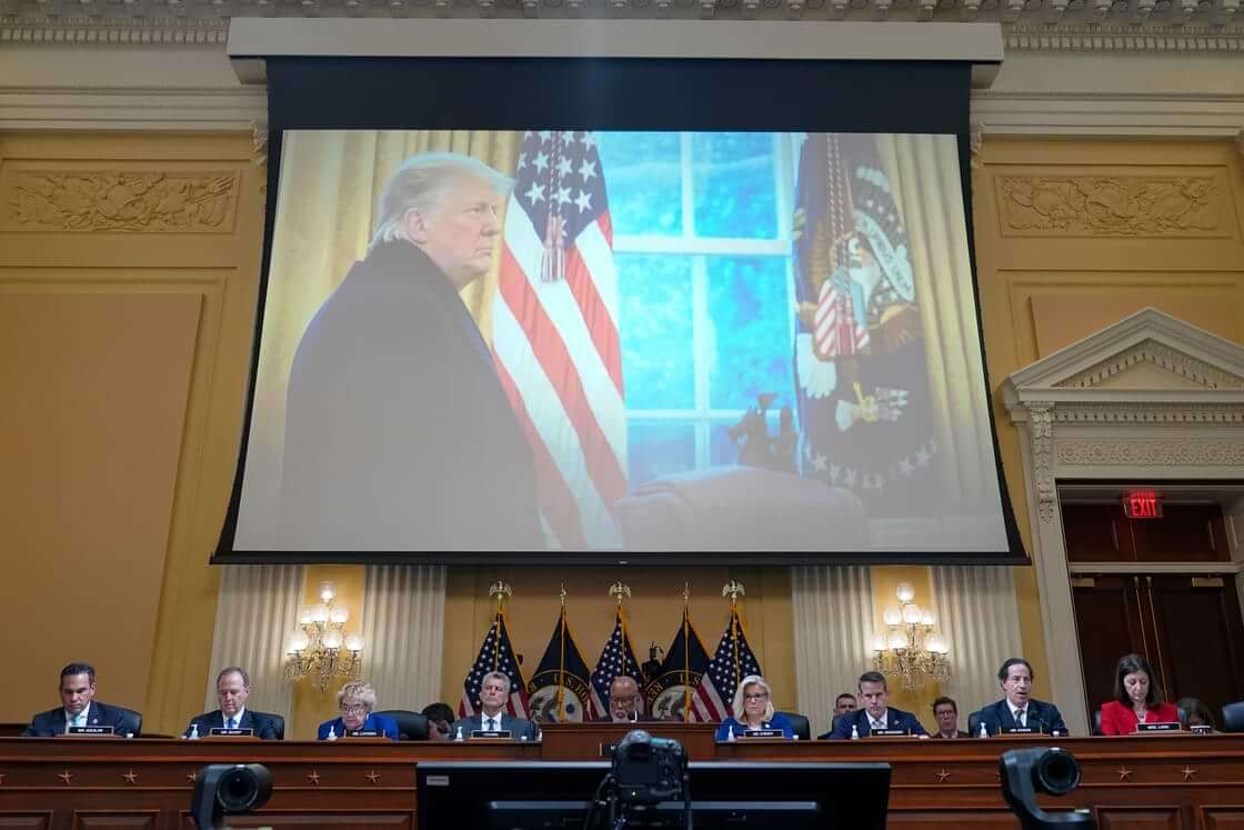 The Jan. 6 committee meets with a projected image of then-president Donald Trump behind and above them.