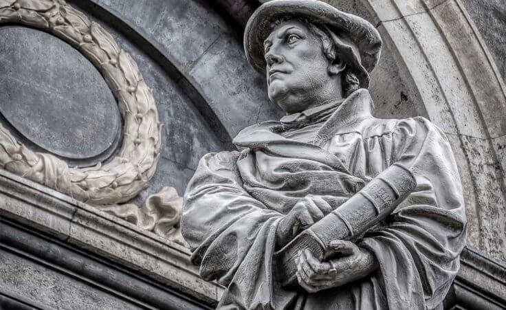 A statute of Martin Luther holding a Bible in one hand and pointing to its cover with his other hand outside of a Copenhagen church.