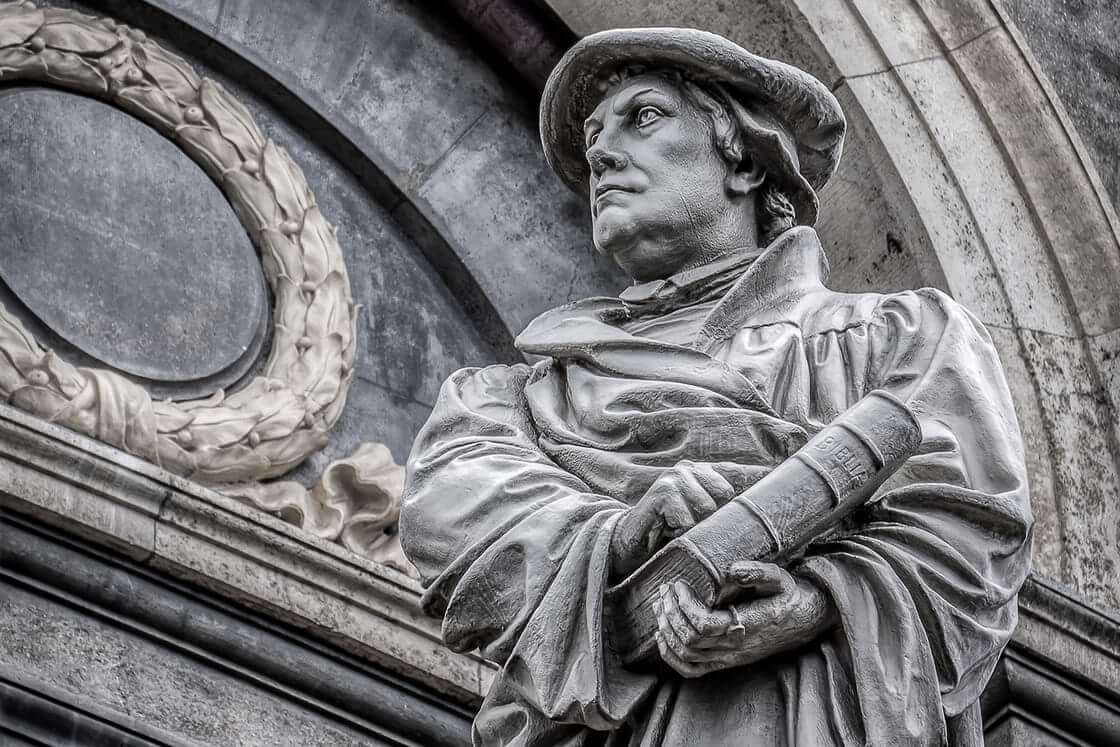 A statute of Martin Luther holding a Bible in one hand and pointing to its cover with his other hand outside of a Copenhagen church.