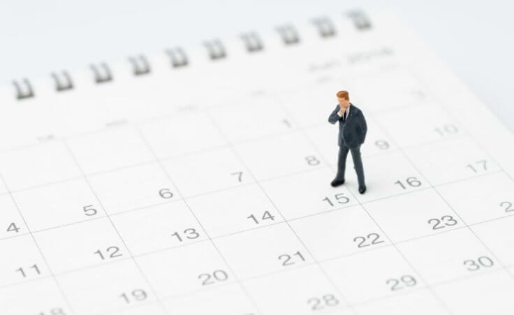 A miniature figurine of a man in a thoughtful pose stands on a calendar page. © Nuthawut/stock.adobe.com