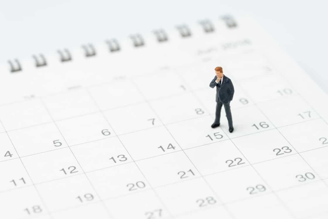 A miniature figurine of a man in a thoughtful pose stands on a calendar page. © Nuthawut/stock.adobe.com