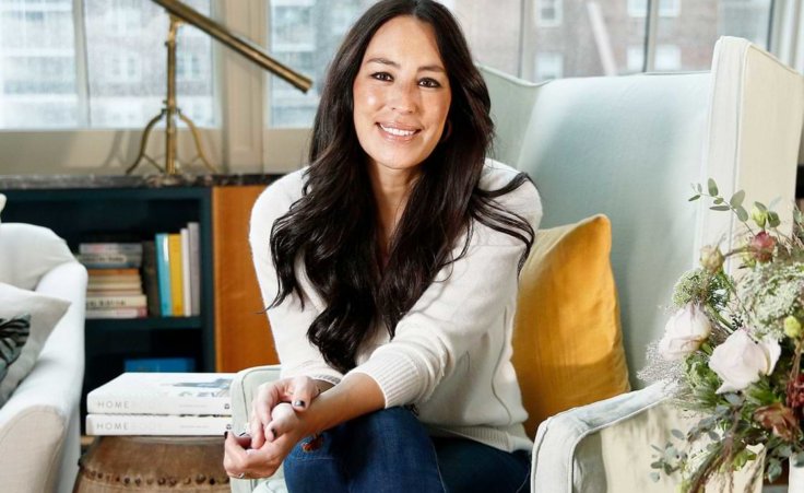Joanna Gaines of Fixer Upper fame sits on a chair in a well-decorated room