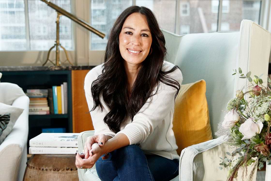 Joanna Gaines of Fixer Upper fame sits on a chair in a well-decorated room
