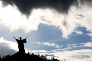A Moses-like silhouette stands on a mountain with both arms upraised