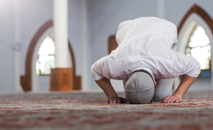 A Muslim man prays with his forehead and hands touching the floor.