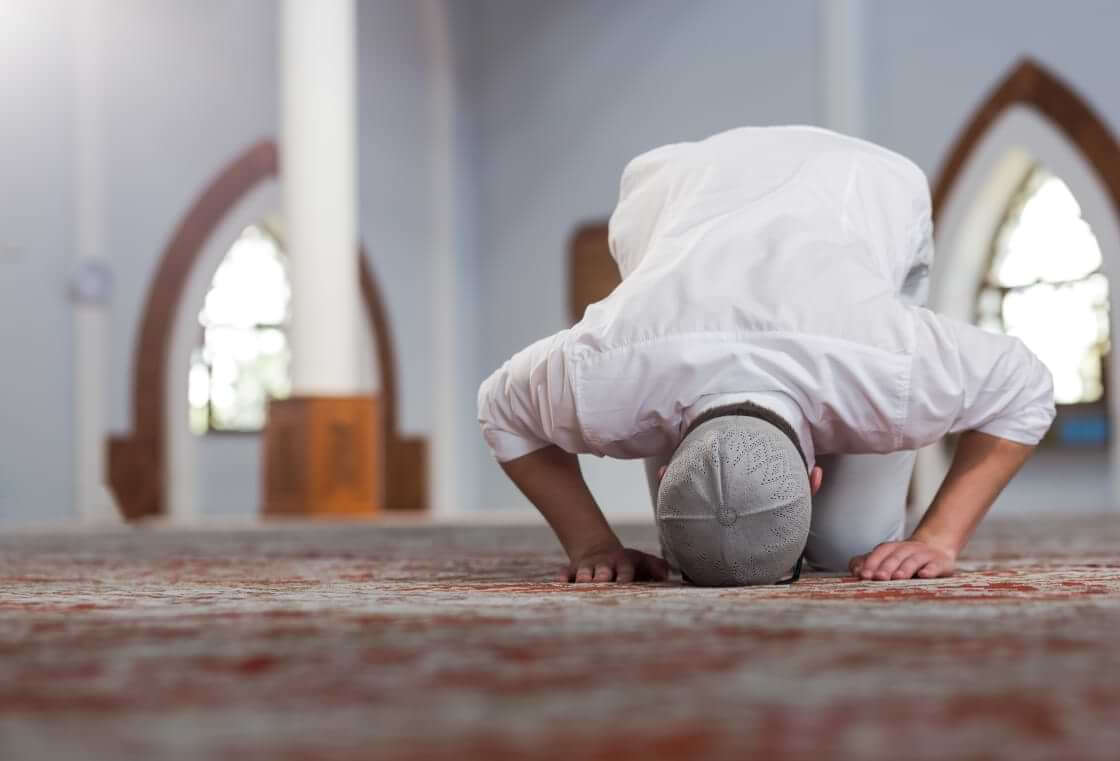 A Muslim man prays with his forehead and hands touching the floor.
