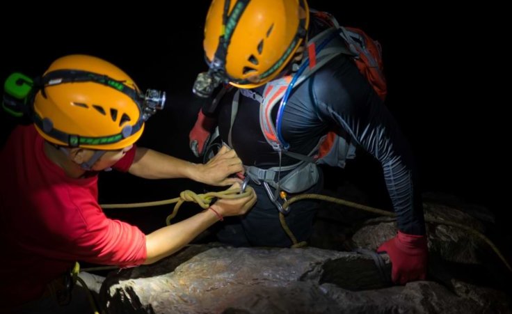 Stock photo: One cave explorer helps another by tightening a rope around a climbing hook.