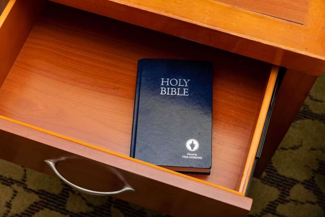 A Gideon's Bible sits in an open drawer inside of a hotel room.