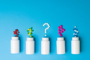 Pills are spilled from five bottles of medicine, with the pills from the central bottle forming a question mark. © By AntonioDiaz/stock.adobe.com