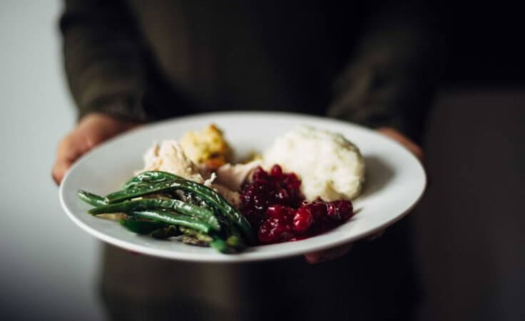 A woman holds a plate of Thanksgiving dinner. © By Laura/stock.adobe.com