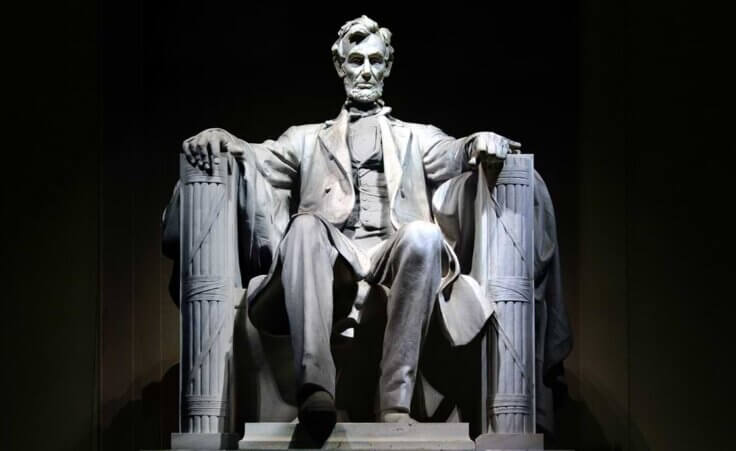 Light shines upon the Abraham Lincoln memorial statue against a black background.