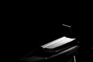 In a black-and-white image, an open Bible sits on a lectern, a single light shining down on it.