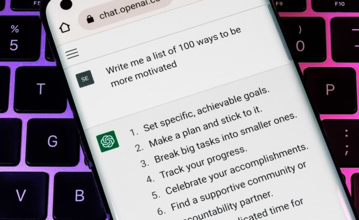 A mobile phone screen shows the Open AI ChatGPT interface with the user's query at the top: "Write me a list of 100 ways to be more motivated" and the artificial intelligence's first six answers. © By Ascannio/stock.adobe.com