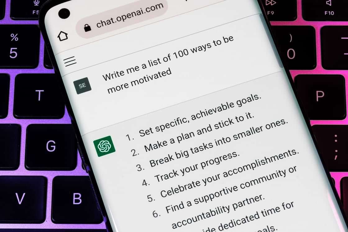 A mobile phone screen shows the Open AI ChatGPT interface with the user's query at the top: "Write me a list of 100 ways to be more motivated" and the artificial intelligence's first six answers. © By Ascannio/stock.adobe.com