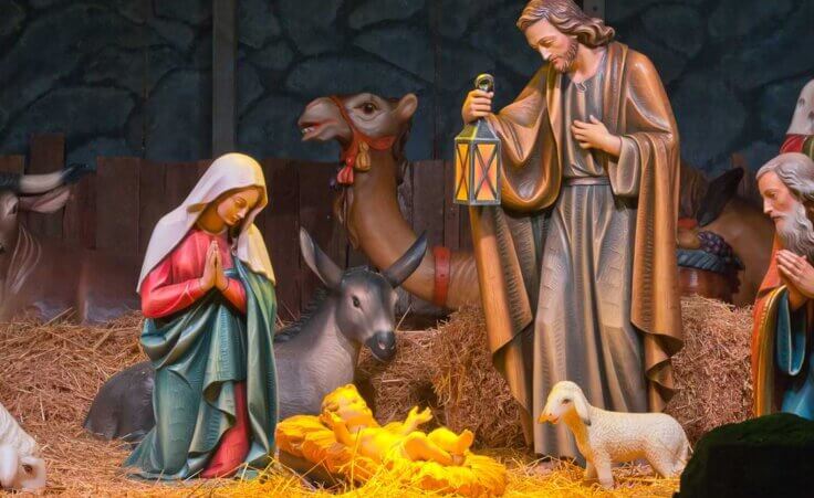 A Christmas nativity scene features a standing Joseph and a kneeling Mary surrounding baby Jesus in a manger. © By RG/stock.adobe.com