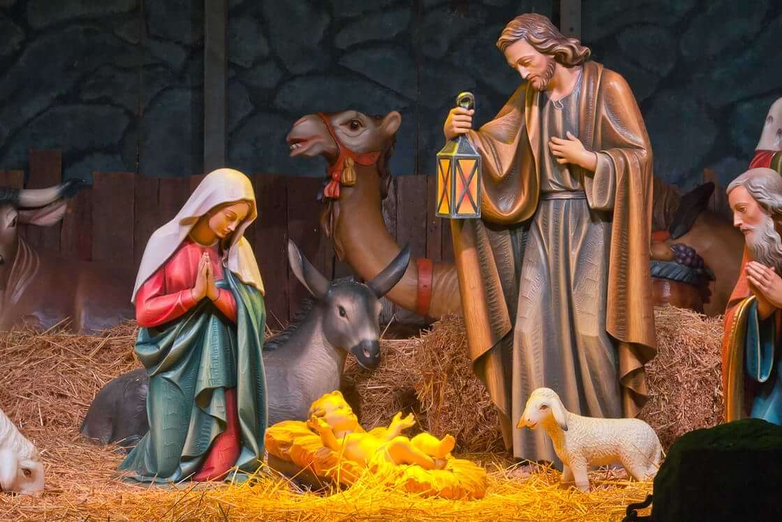 A Christmas nativity scene features a standing Joseph and a kneeling Mary surrounding baby Jesus in a manger. © By RG/stock.adobe.com