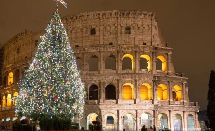 A well-lit Christmas tree stands outside of the Coliseum in Rome, Italy, at night. © By Matteo Gabrieli/stock.adobe.com