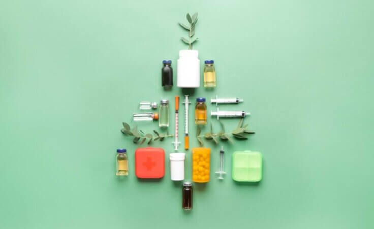 A Christmas tree comprised of vials, bottles, and medicine sits against a green background.