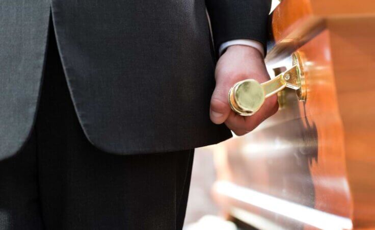 A coffin bearer holds the brass handle to a casket. © By Kzenon/stock.adobe.com