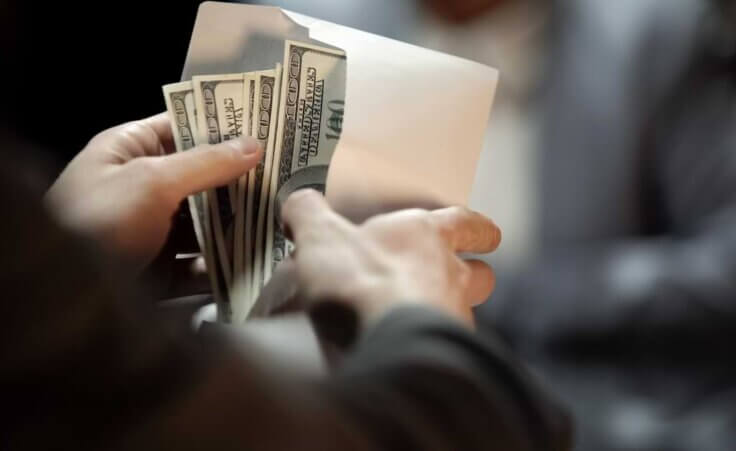 A person opens a white envelope filled with hundred-dollar bills.