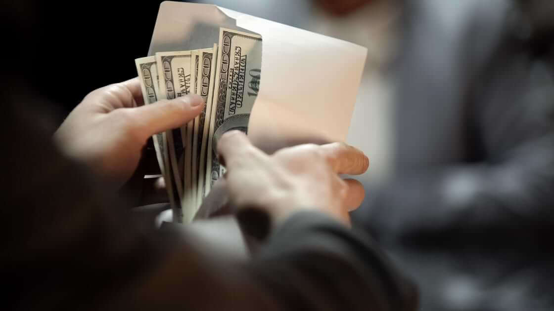 A person opens a white envelope filled with hundred-dollar bills.