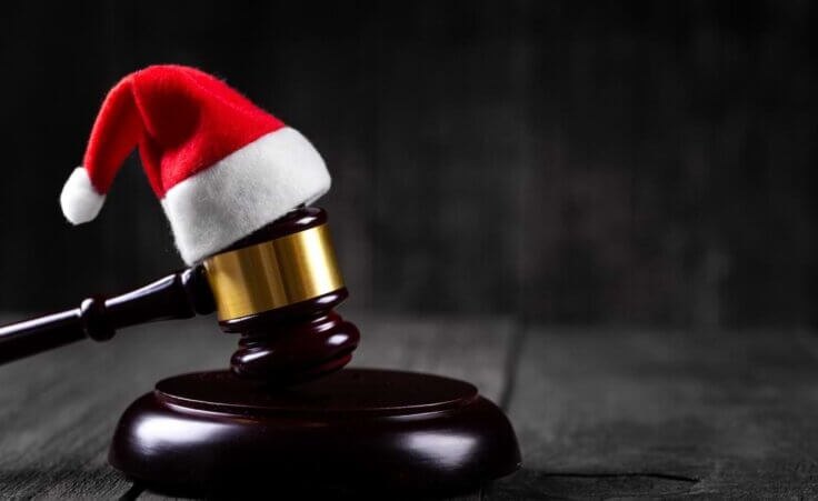 A Santa Claus hat sits atop a gavel against a wooden rustic background