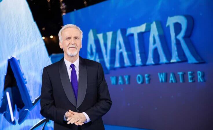 James Cameron stands in front of an Avatar: The way of water banner