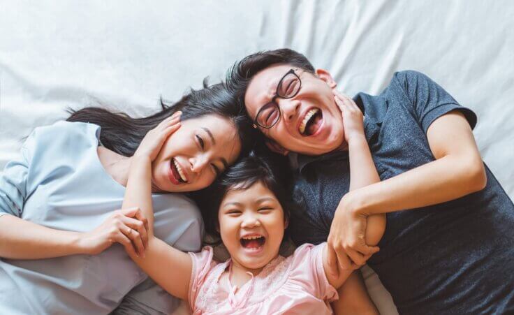 Happy parents and daughter all laughing together © By Nattakorn /stock.adobe.com | A stock photo for a book review of Habits of the Household