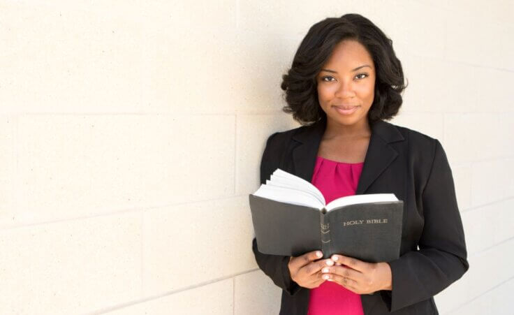 A woman holds a Bible open while looking straight ahead. © By pixelheadphoto/stock.adobe.com