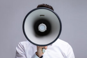 A man in white shirt holds a megaphone toward the camera. © By Andrey Popov/stock.adobe.com. In the West, Christian persecution can often look like attacks on your belief or character.