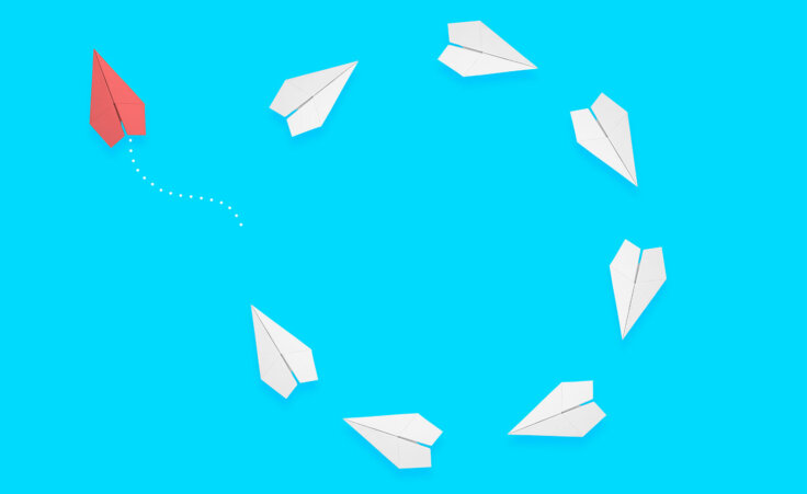 Seven white paper airplanes form a circle, but a single red paper airplane chooses its own path, flying up and to the left. © By Memed ÖZASLAN/stock.adobe.com