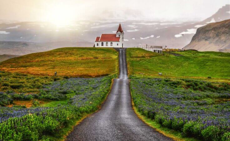 A long road leads to a lone white church in Hellissandur, Iceland. © Blue Planet Studio/stock.adobe.com